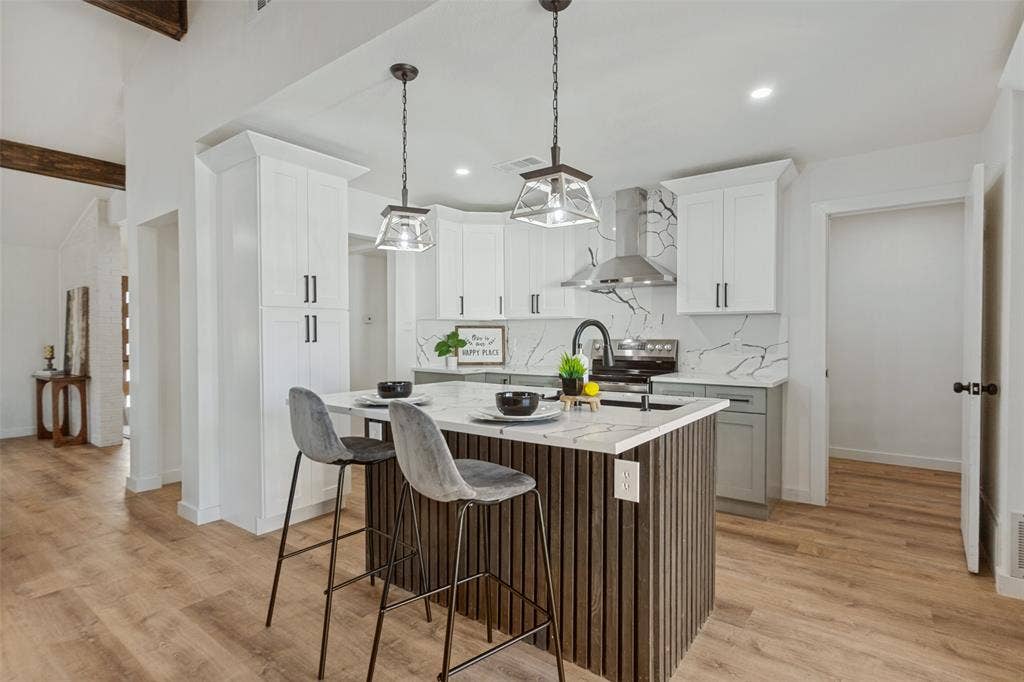 828 Melrose Drive, Richardson, TX 75234 Kitchen featuring white shaker-style cabinetry, quartz countertops with integrated backsplash, wood-finish flooring, a vertical-slat kitchen island, and dual pendant lighting