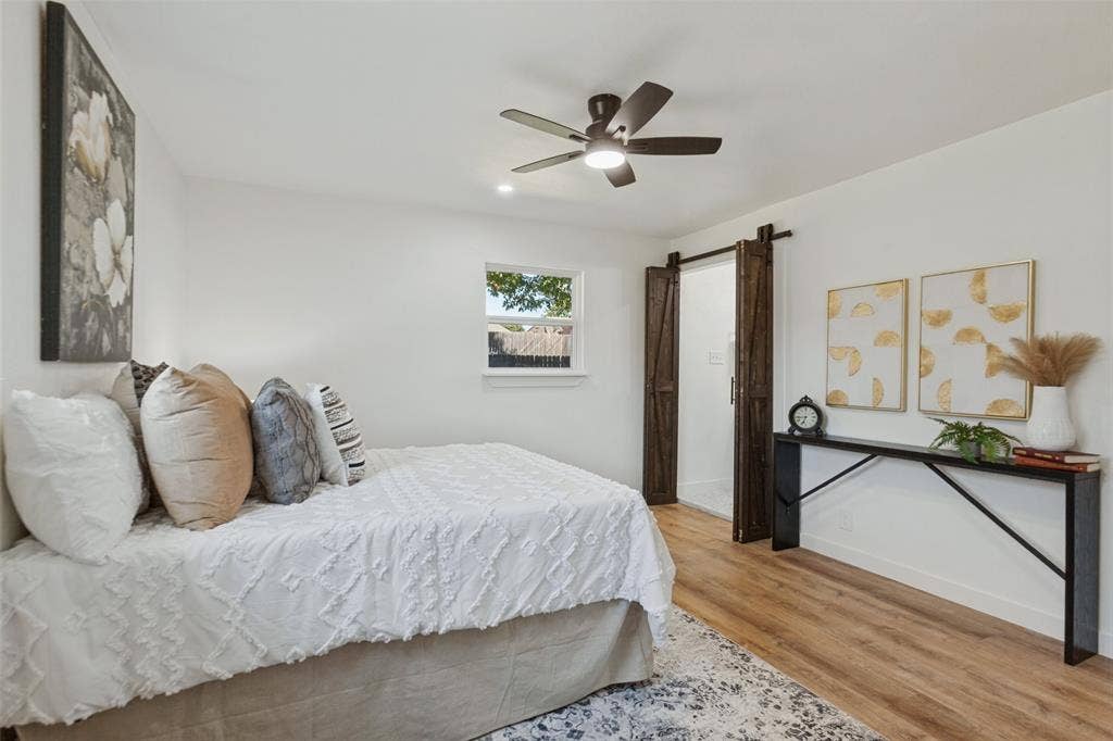 828 Melrose Drive, Richardson, TX 75234 Interior room featuring wood-finish flooring, a five-blade ceiling fan with integrated lighting, and dark wood-finish sliding barn doors