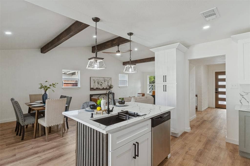 828 Melrose Drive, Richardson, TX 75234 Kitchen featuring a central island with a stone-patterned countertop, dark metal hardware, wood-finish flooring, exposed ceiling beams, and pendant lighting