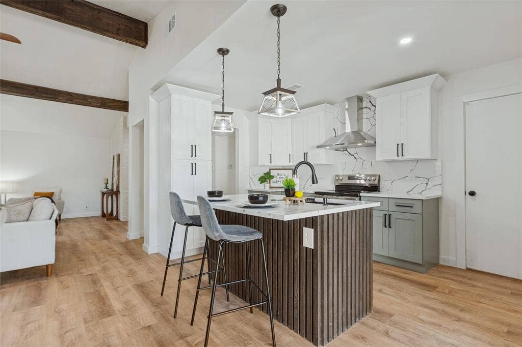 828 Melrose Drive, Richardson, TX 75234 Kitchen featuring wood-finish flooring, a central island with vertical wood slat detailing, stone-patterned backsplash, white shaker cabinetry, and stainless steel range hood