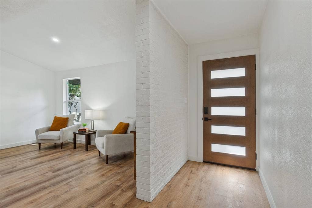 828 Melrose Drive, Richardson, TX 75234 Entryway featuring a wood-finish front door with horizontal frosted glass panels, white painted brick accent wall, and wood-finish flooring