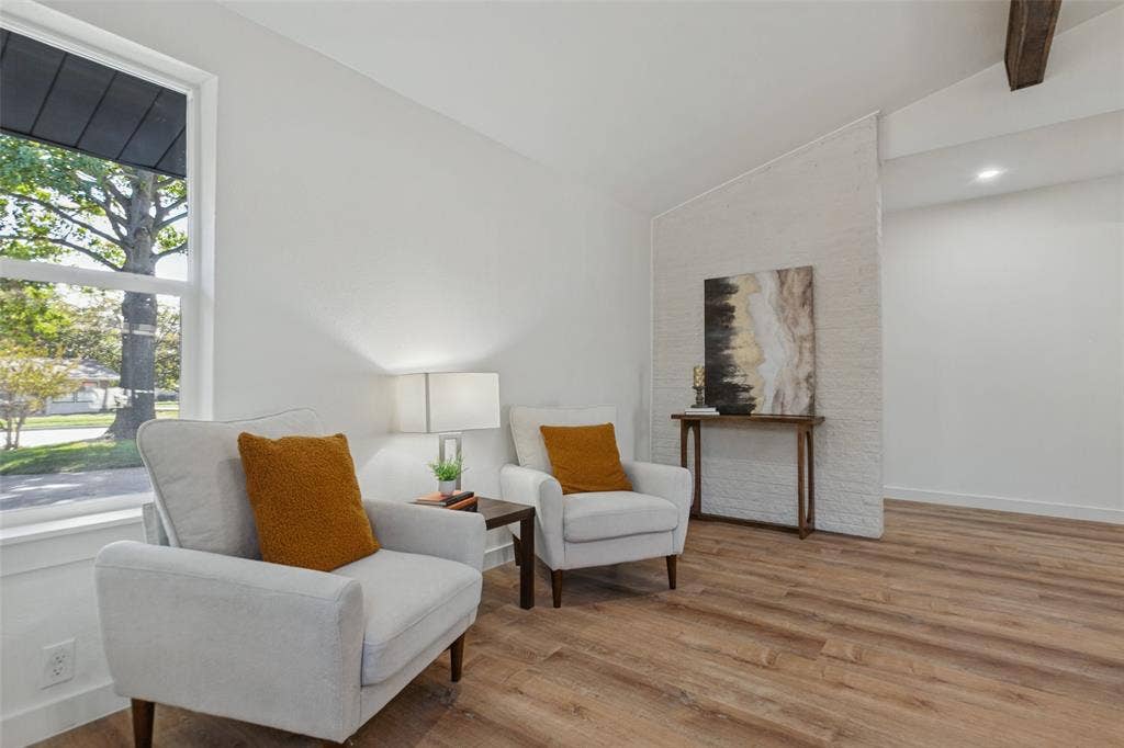 828 Melrose Drive, Richardson, TX 75234 Vaulted ceilings featuring wood-finish beams, white painted brick accent wall, wood-finish flooring, and expansive windows