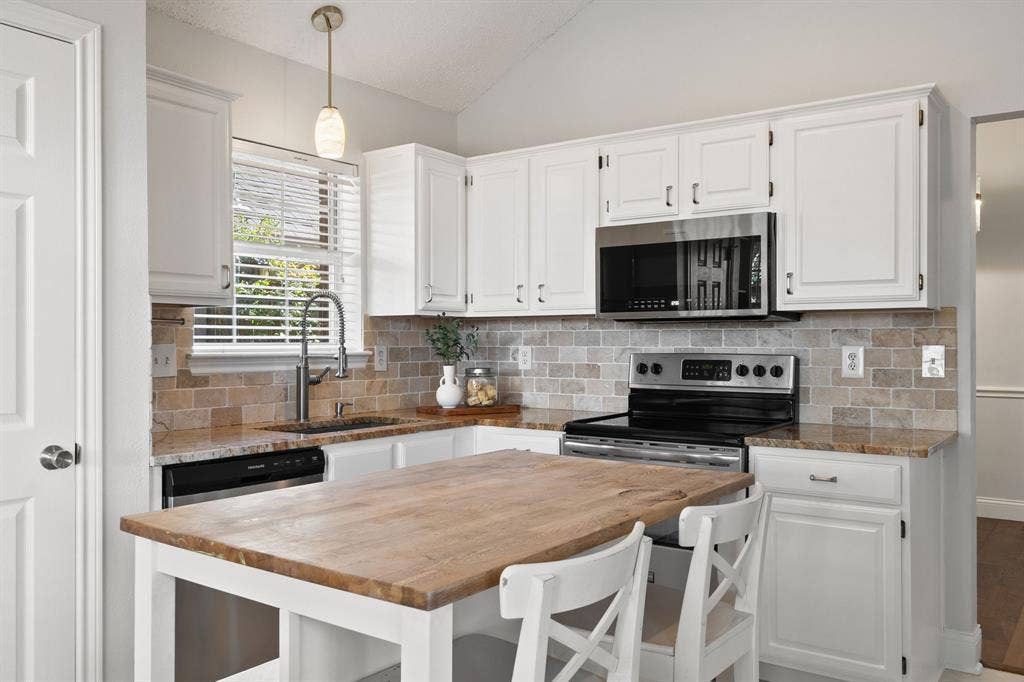 11414 Ocean Road, Frisco, TX 75035 Kitchen featuring white shaker-style cabinetry, stone tile backsplash, stone countertops, stainless steel appliances, and a central island with a wood surface