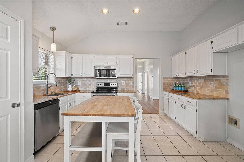 11414 Ocean Road, Frisco, TX 75035 Kitchen featuring white cabinetry, stone-finish countertops, stainless steel appliances, brick-style backsplash, and a central island with a wood surface