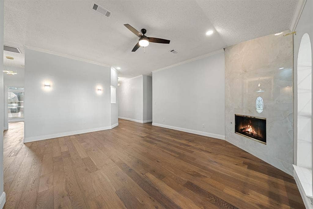 11414 Ocean Road, Frisco, TX 75035 Living area featuring wood-finish flooring, a stone-surround fireplace, crown molding, a ceiling fan with light kit, and wall-mounted sconces