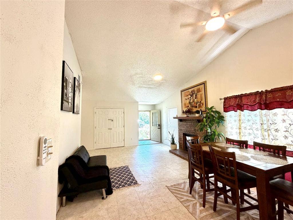 817 Colchester Drive, Mesquite, TX 75149 Living and dining area featuring vaulted ceilings, a ceiling fan with integrated lighting, a brick fireplace with a wood mantle, and light-toned tile flooring