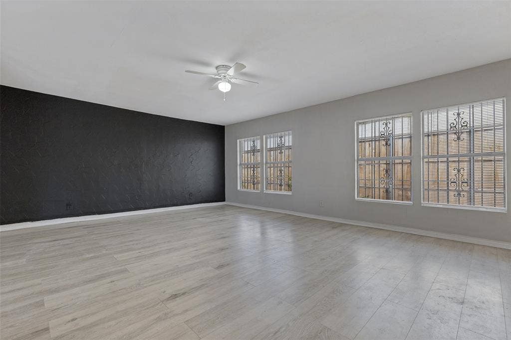 6719 Kenwell Street, Dallas, TX 75209 Interior space featuring wood-finish flooring, a textured accent wall, four windows with exterior security bars, and a ceiling fan with integrated lighting