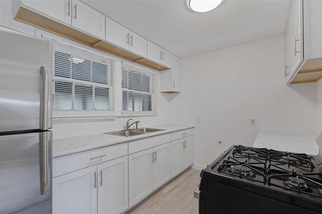 6719 Kenwell Street, Dallas, TX 75209 Kitchen featuring white shaker-style cabinetry, stainless steel appliances, double-basin sink with a gooseneck faucet, and light-toned wood-finish flooring