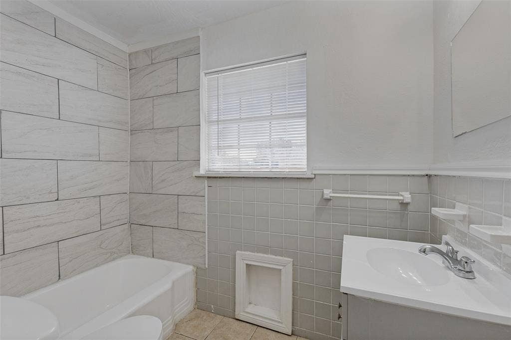 6719 Kenwell Street, Dallas, TX 75209 Bathroom featuring a tub with large-format wall tile, square wall-tile surround, vanity with an integrated sink, polished metal hardware, and a wall-mounted towel bar