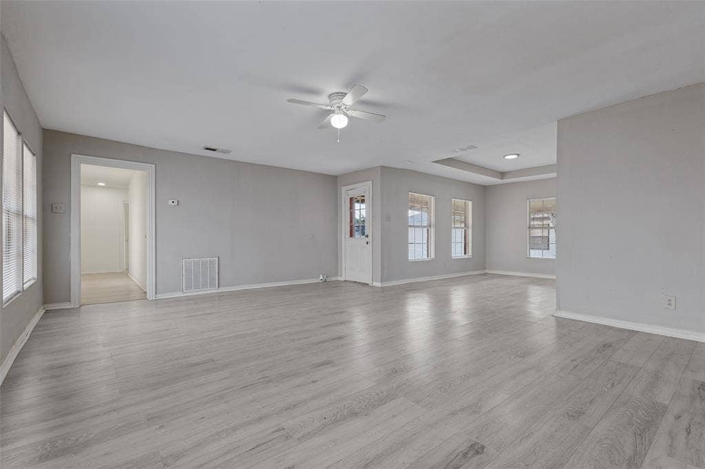 6719 Kenwell Street, Dallas, TX 75209 Neutral-toned interior space featuring wood-finish flooring, a tray ceiling, multiple windows, and a ceiling fan with integrated light fixture