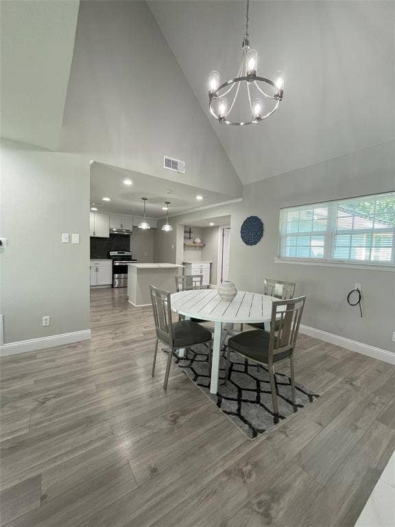 Dining space featuring an inviting chandelier, high vaulted ceiling, and light wood-type flooring