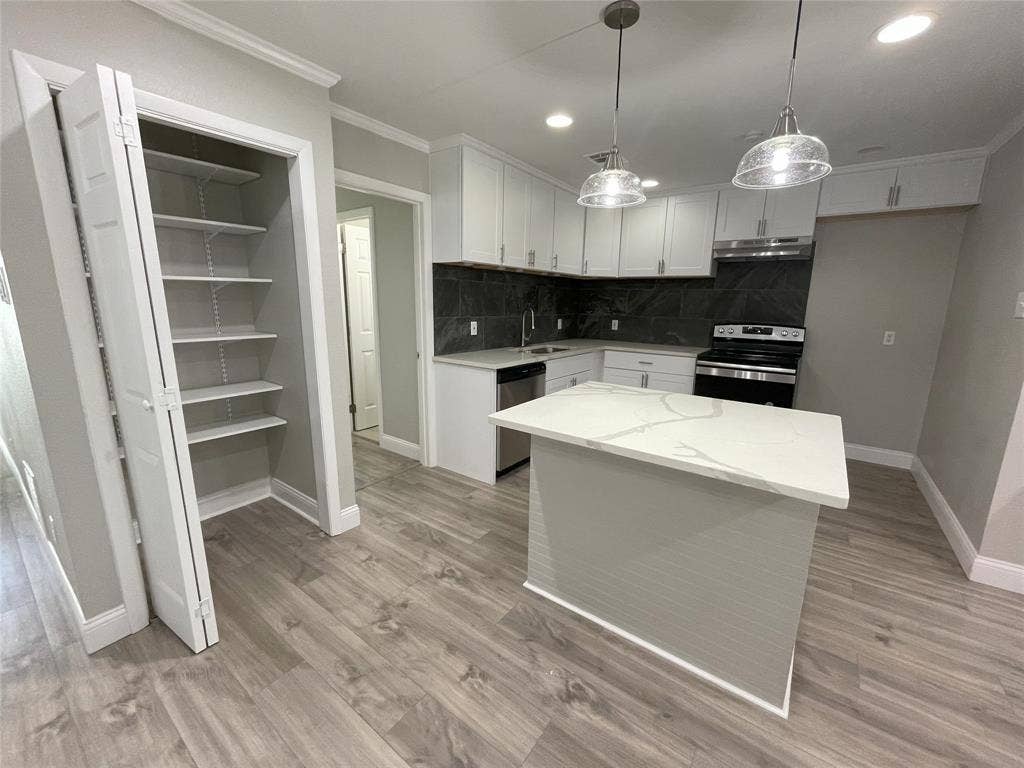 Kitchen with appliances with stainless steel finishes, light hardwood / wood-style flooring, tasteful backsplash, white cabinets, and a center island