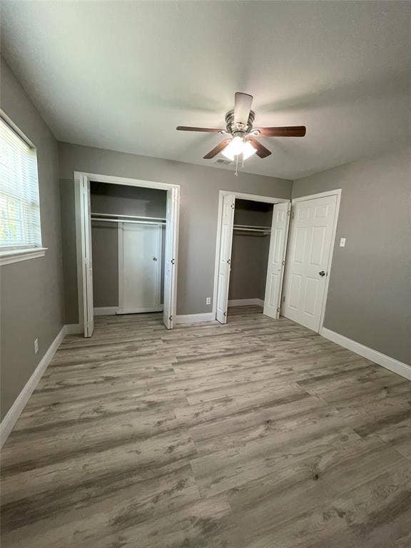 Unfurnished bedroom featuring multiple closets, ceiling fan, and hardwood / wood-style flooring