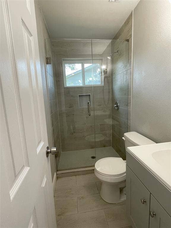 Bathroom with walk in shower, tile patterned floors, toilet, and vanity