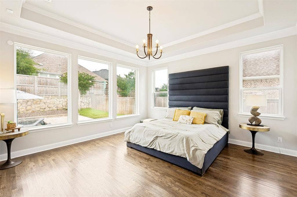 1730 Cottonwood Trail, Prosper, TX 75078 Spacious primary suite room featuring wood flooring, a tray ceiling with a central chandelier and great views of the backyard oasis.