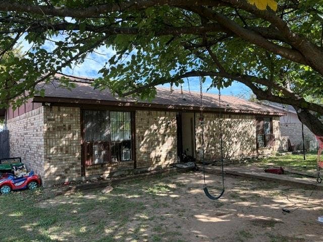 10311 Kinslow Drive, Dallas, TX 75217 Single-story brick exterior featuring a composition shingle roof, mature canopy trees, and dark-finished window frames