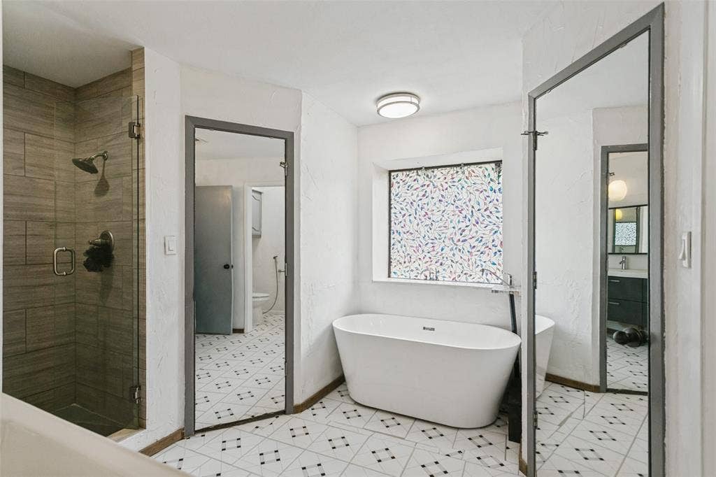 8820 Woodstream Drive, Frisco, TX 75034 Freestanding soaking tub, walk-in shower with wood-finish tile surround, glass shower enclosure, and patterned tile flooring