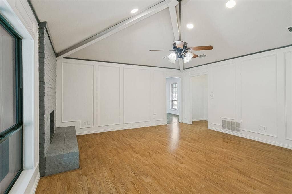 8820 Woodstream Drive, Frisco, TX 75034 Vaulted ceiling with exposed structural beams, wood-finish flooring, painted brick fireplace, and wall paneling detail
