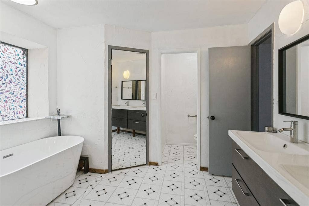 8820 Woodstream Drive, Frisco, TX 75034 Freestanding soaking tub, dual-sink vanity with dark cabinetry, patterned tile flooring, and decorative leaded glass window