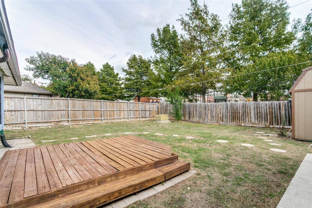 8820 Woodstream Drive, Frisco, TX 75034 Backyard featuring a tiered wooden deck, perimeter wood fencing, mature trees, and stone paver path