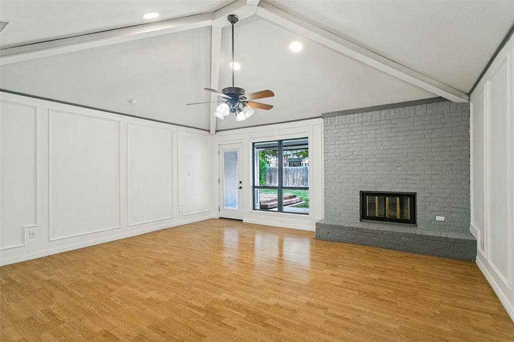 8820 Woodstream Drive, Frisco, TX 75034 Vaulted ceiling with exposed beams, wood-finish flooring, floor-to-ceiling wainscoting, and a painted brick fireplace with an elevated hearth