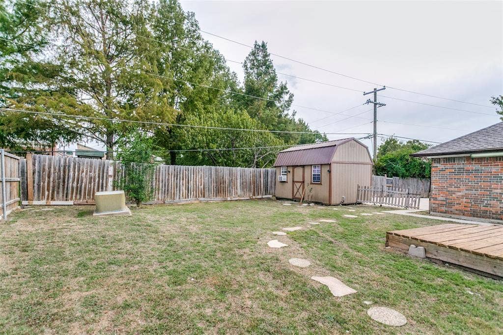 8820 Woodstream Drive, Frisco, TX 75034 Backyard featuring a wood-style shed, natural stone paver pathway, brick exterior siding, and a wooden ground-level deck, enclosed by perimeter wood fencing