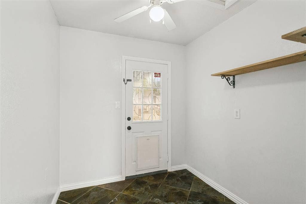 8820 Woodstream Drive, Frisco, TX 75034 Entryway featuring diagonal slate flooring, a white door with a decorative glass panel, integrated pet door, and wall-mounted wood shelving with decorative metal brackets, complemented by a ceiling fan with integrated lighting