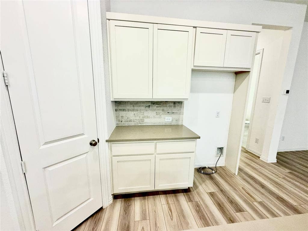 Shaker-style cabinetry in white finish, stone-composite countertop, brick-patterned tile backsplash, and wood-finish flooring
