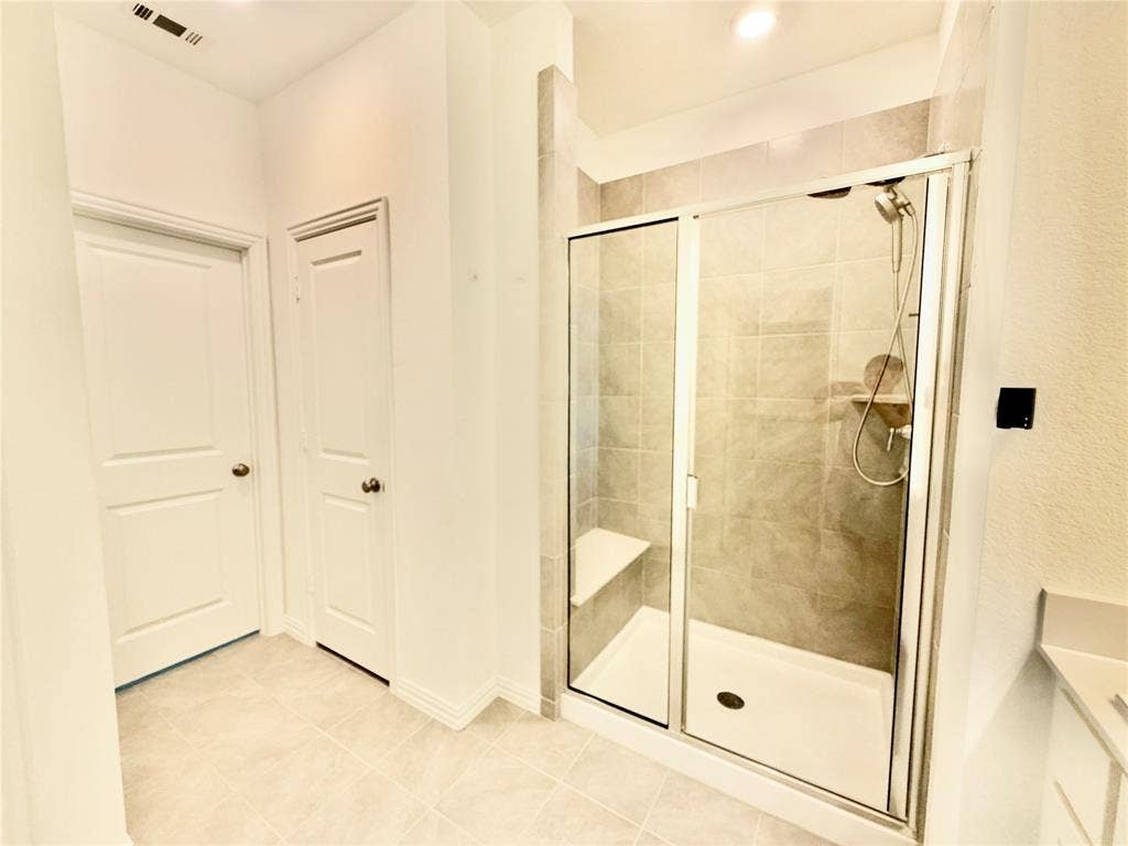 Walk-in shower featuring a glass enclosure, built-in bench seat, ceramic tile surround, and handheld shower fixture, complemented by neutral tile flooring