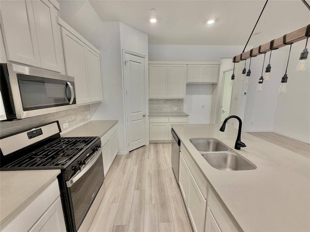 Kitchen featuring white cabinetry, solid-surface countertops, wood-finish flooring, a stainless steel gas range with overhead microwave, and a center island with a dual-basin sink and matte black faucet