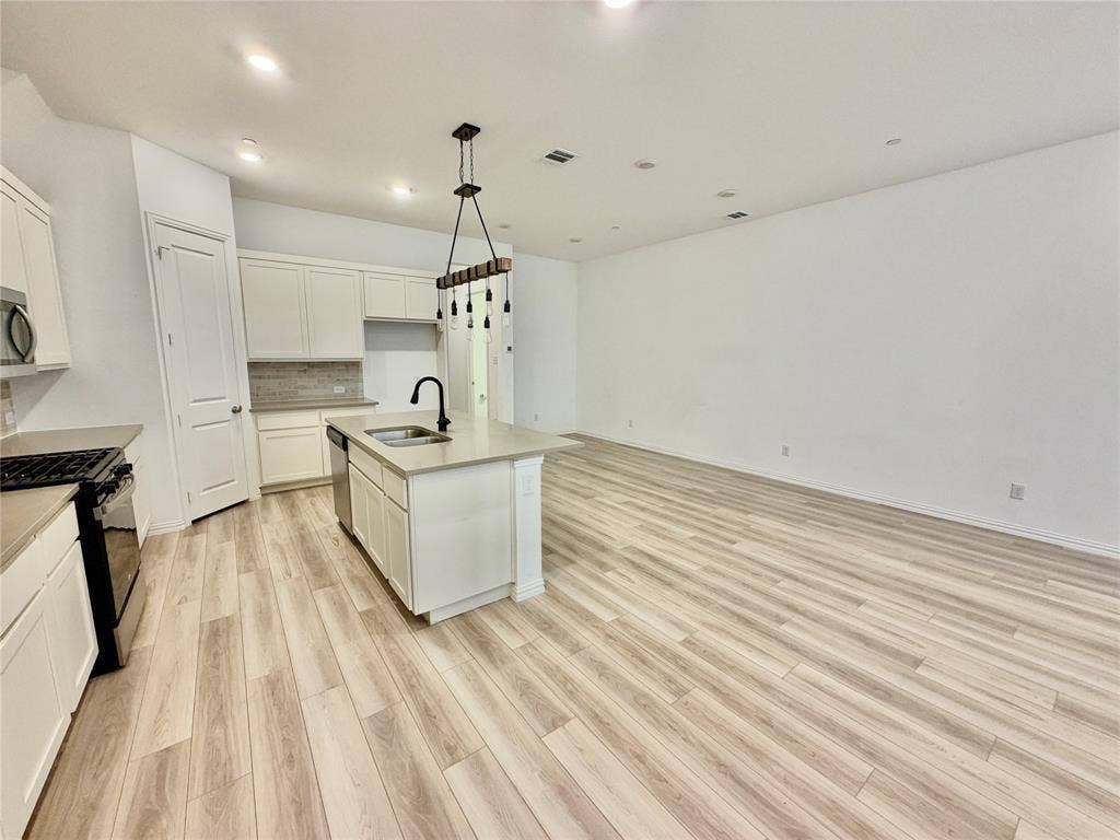 Kitchen featuring wood-finish flooring, a central island with a solid surface countertop, matte black faucet, and pendant lighting