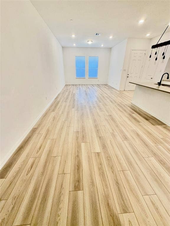 Open-concept space featuring light-toned wood-finish flooring, recessed ceiling lighting, dual windows, and a built-in kitchen peninsula with an integrated sink and matte black faucet