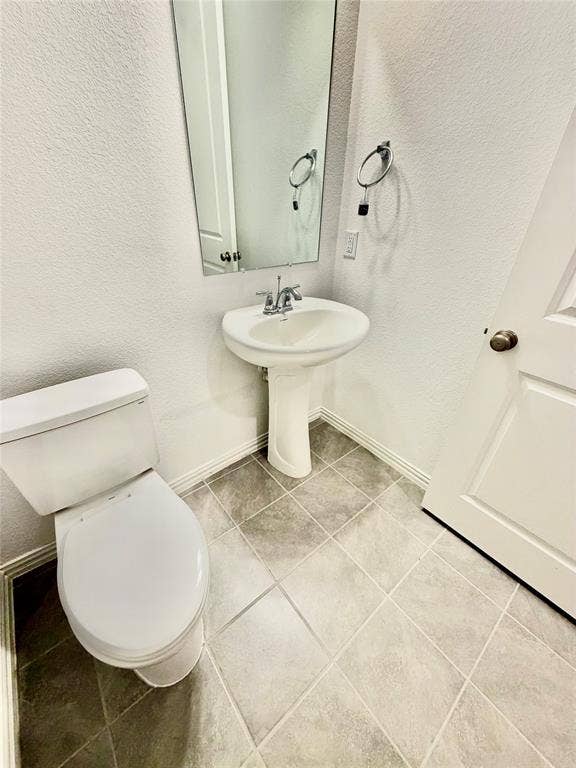 Pedestal sink with a two-handle chrome faucet, rectangular wall-mounted mirror, ceramic tile flooring, and a two-piece white toilet