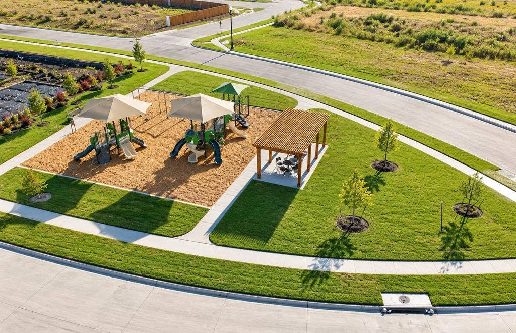 Recreational area featuring a playground with shade structures, a wooden pergola, manicured lawn, and paved walkways