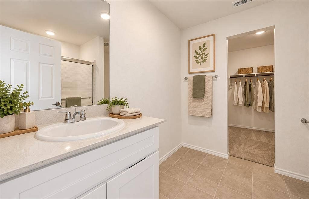 Bathroom featuring a white vanity with a composite countertop, an undermount oval sink, chrome-finish faucet, wall-to-wall mirror, and a walk-in closet with built-in shelving