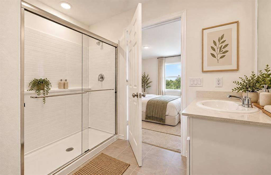 Bathroom featuring a walk-in shower with a glass enclosure, white tile surround, vanity with stone-style countertop, and drop-in sink