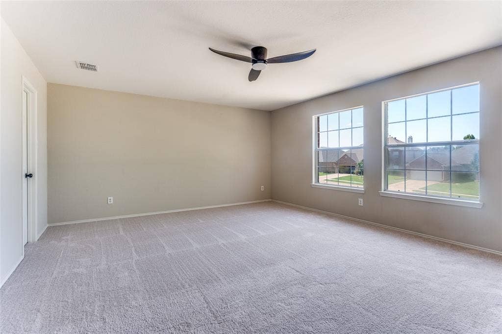 Neutral-toned interior space featuring light-colored wall-to-wall carpeting, dual double-pane windows, and a multi-blade ceiling fan