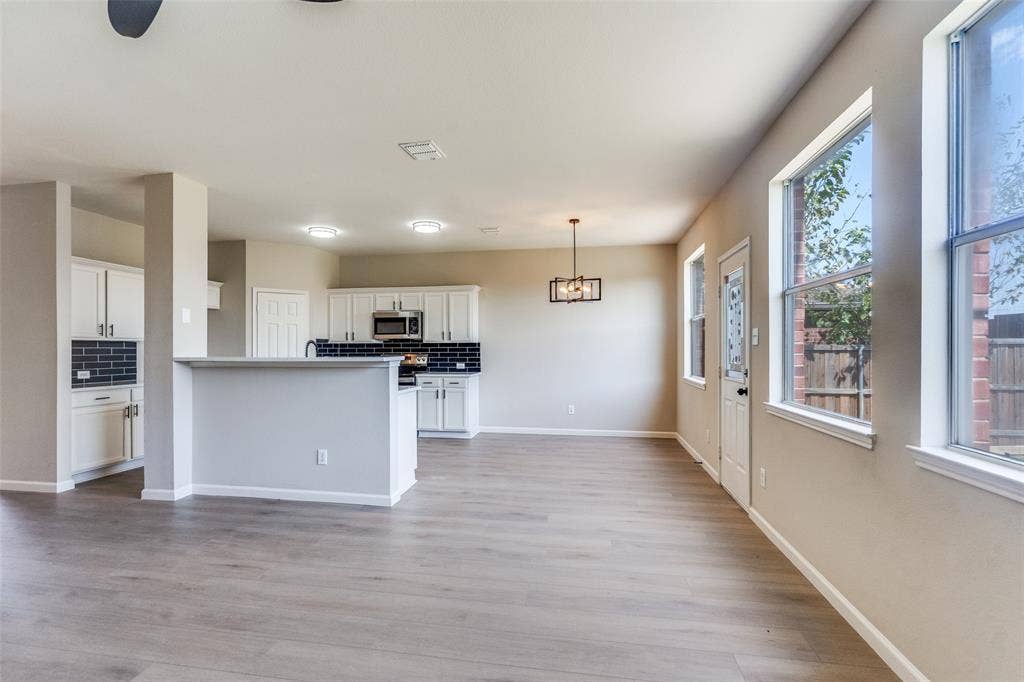 Kitchen featuring white cabinetry, dark tile backsplash, stainless steel microwave, wood-finish flooring, and a pendant light fixture