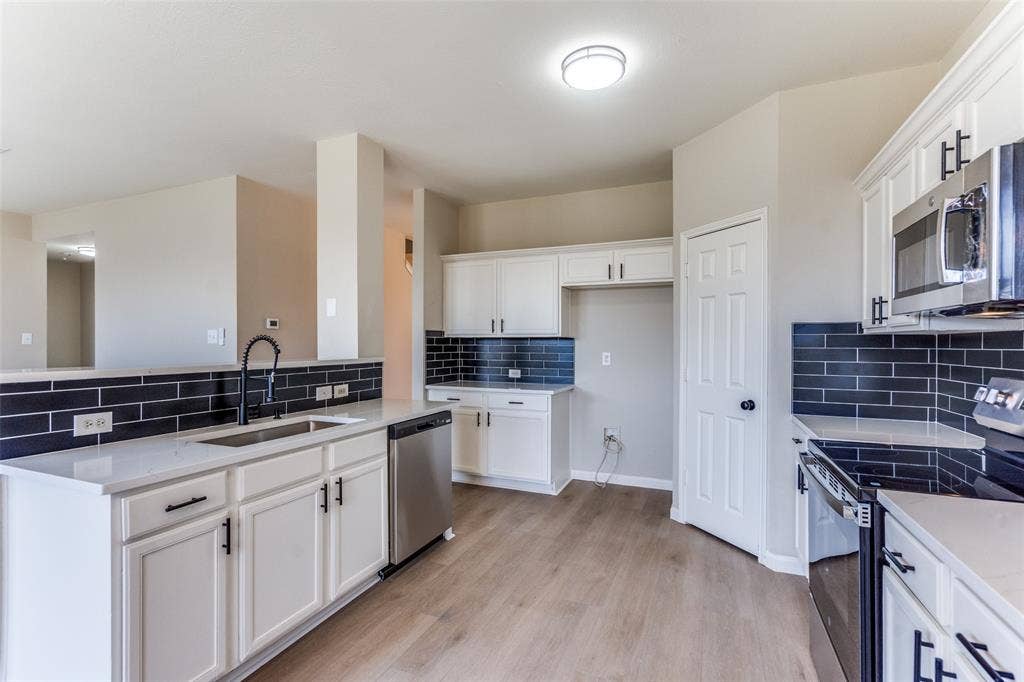 Kitchen featuring white cabinetry with matte black hardware, stone-finish countertops, black subway tile backsplash, stainless steel appliances, and wood-finish flooring