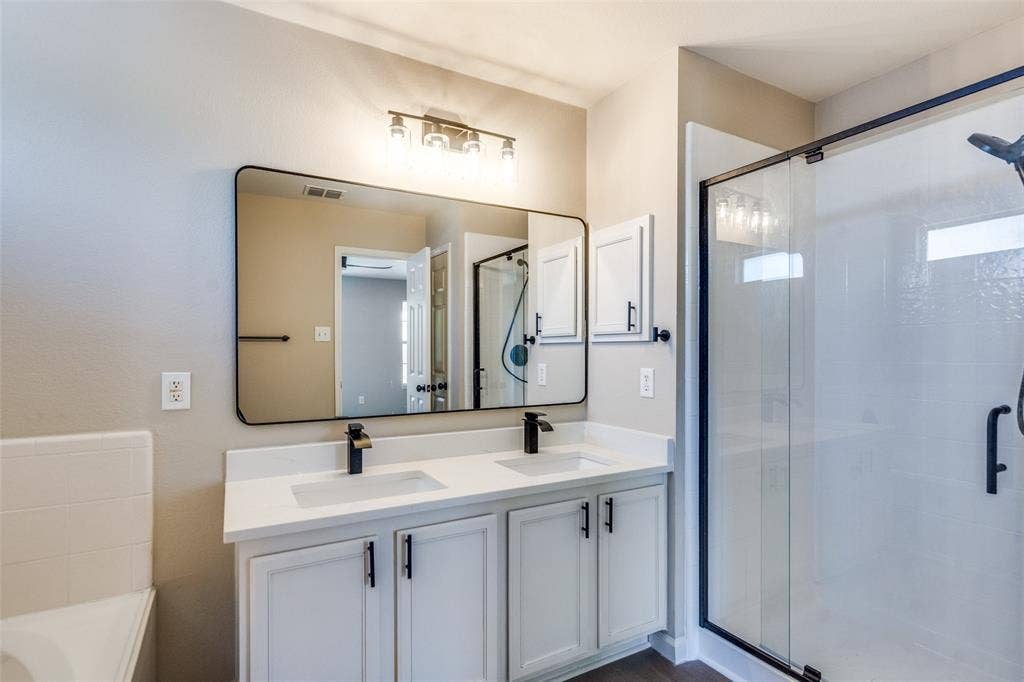 Double vanity featuring white cabinetry, quartz-style countertops, rectangular undermount sinks, matte black hardware, and a framed mirror