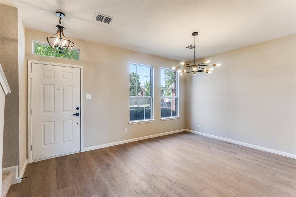 Wood-finish flooring, multi-light modern chandelier, globe-style pendant light, transom window, and dual double-pane windows