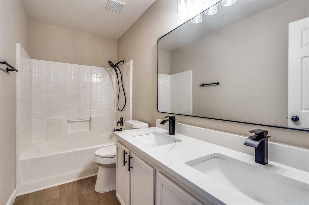 Dual vanity with a white composite countertop, undermount sinks, matte black widespread faucets, large rectangular wall mirror, and wood-finish flooring