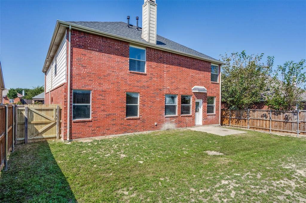 Two-story exterior featuring red brick masonry, a vertical chimney, a rear patio, and enclosed wood fencing