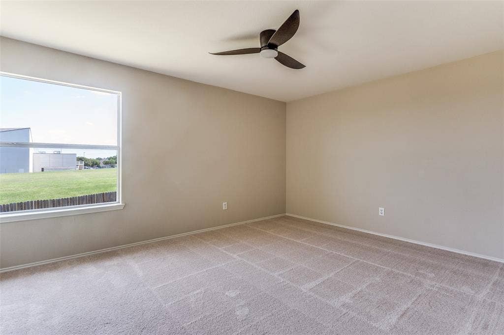 Neutral-toned interior featuring wall-to-wall carpeting, a multi-blade ceiling fan, and a large window with natural light