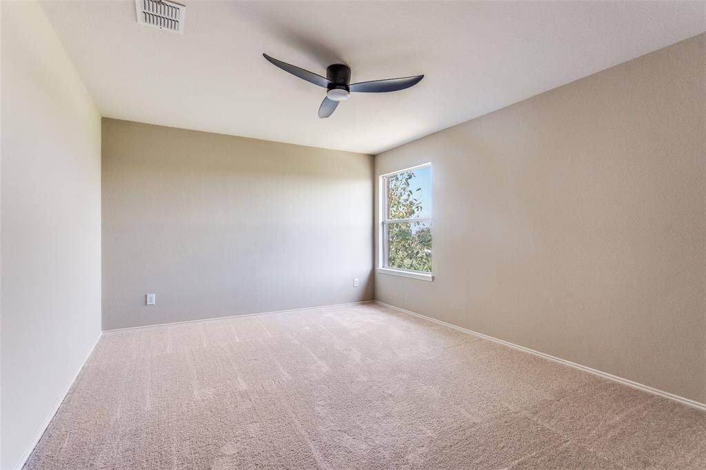 Neutral-toned interior space featuring carpeting, a single-pane window, and a three-blade matte black ceiling fan