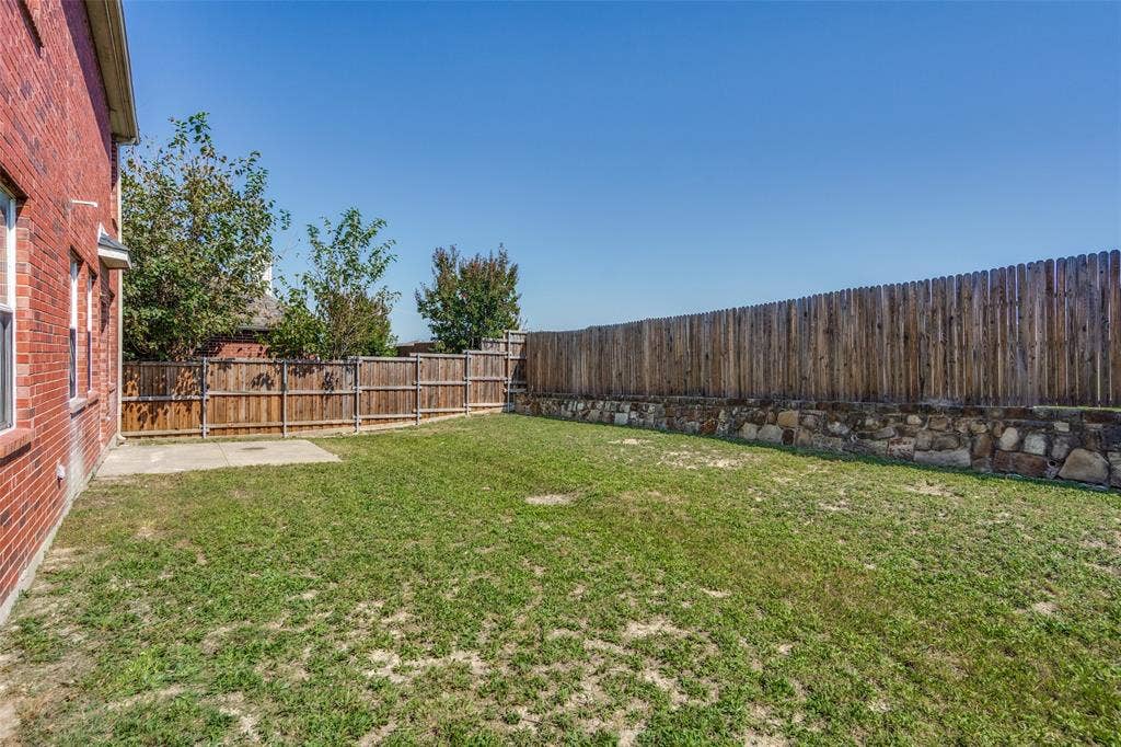 Backyard featuring a red brick exterior, concrete patio, full-height wood privacy fencing, and stone retaining wall