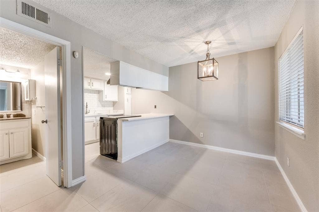 5623 Harvest Hill Road, #2023, Dallas, TX 75230 Open-concept area featuring neutral wall paint, tile flooring, a geometric pendant light fixture, a breakfast bar with white cabinetry, and horizontal window blinds