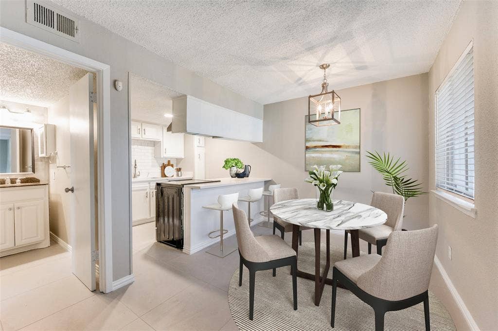 5623 Harvest Hill Road, #2023, Dallas, TX 75230 Kitchen featuring a breakfast bar, white cabinetry, and tile flooring, paired with an eating area highlighted by a geometric pendant light fixture and horizontal blinds