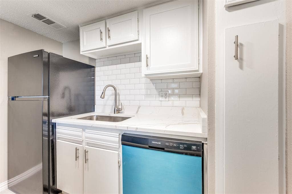5623 Harvest Hill Road, #2023, Dallas, TX 75230 Kitchenette featuring white shaker-style cabinetry, stone-surface countertops, white subway tile backsplash, stainless steel sink with gooseneck faucet, and stainless steel appliances