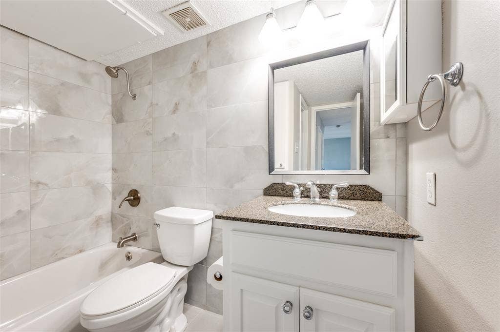 5623 Harvest Hill Road, #2023, Dallas, TX 75230 Bathroom featuring full-height floor to ceiling tile surround, white cabinetry, speckled stone vanity countertop, oval under-mount sink, and framed vanity mirror